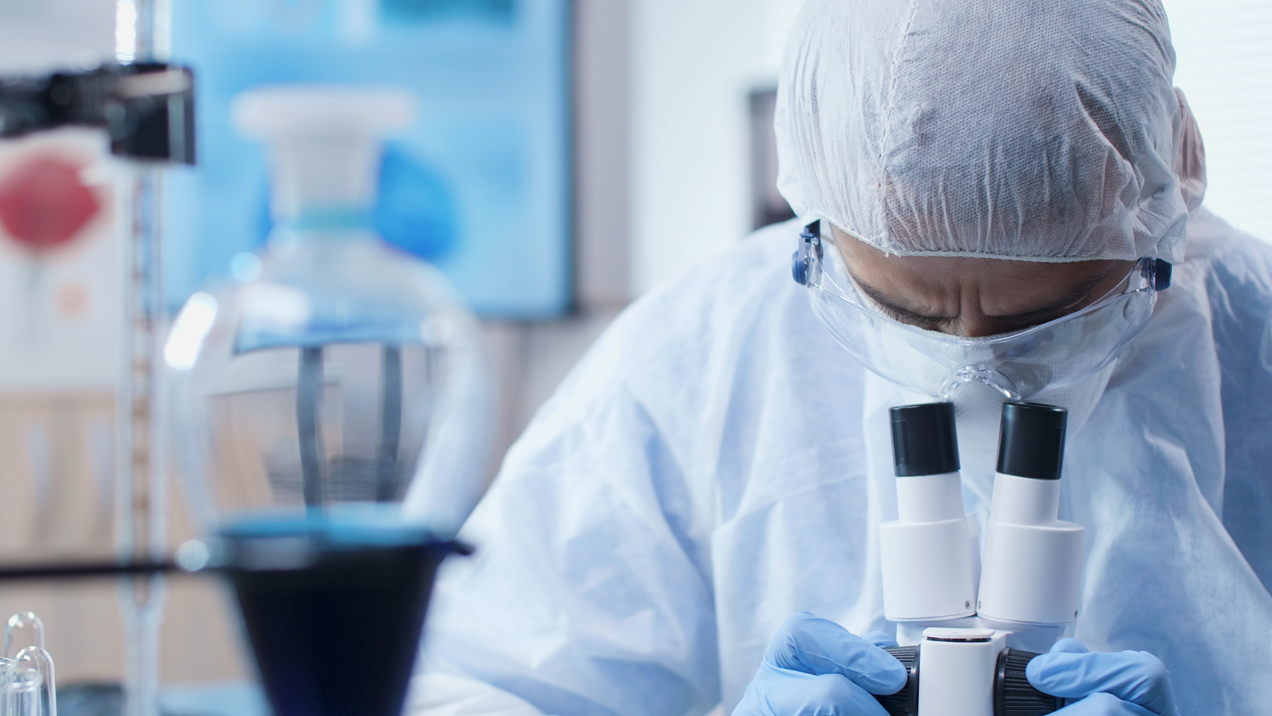 a person in a white protective suit looking through a microscope